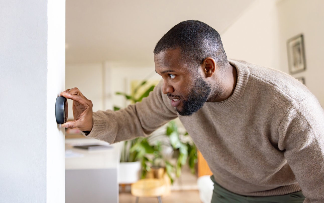 A photo of a man using a thermostat to change the temperature in his home.