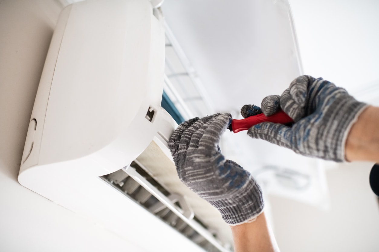 An HVAC repairman works on an AC unit.